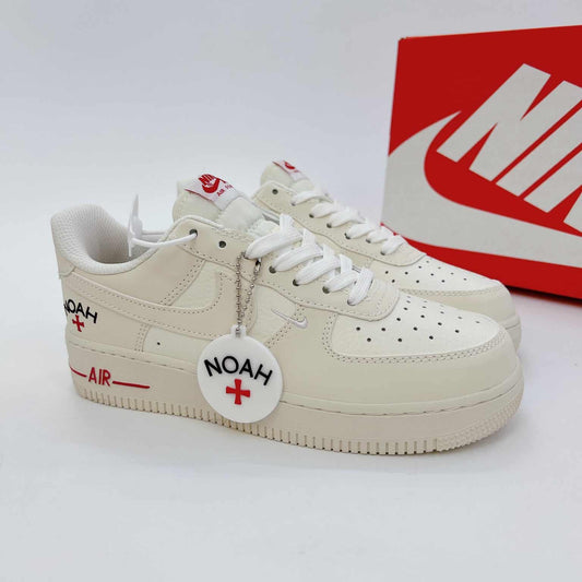 These cream-white Nike Air Force 1 sneakers feature red "Noah" branding accents and a matching circular logo keychain