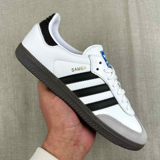 The Adidas Originals Samba OG sneaker features a crisp white leather upper accented by black serrated three-stripes and a classic translucent gum rubber sole