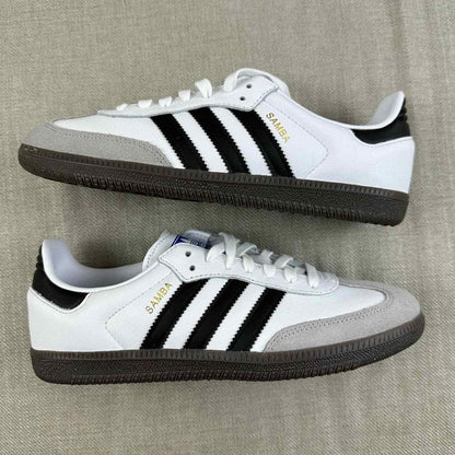 The Adidas Originals Samba OG sneaker features a crisp white leather upper accented by black serrated three-stripes and a classic translucent gum rubber sole