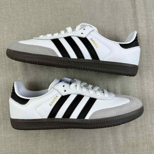 The Adidas Originals Samba OG sneaker features a crisp white leather upper accented by black serrated three-stripes and a classic translucent gum rubber sole